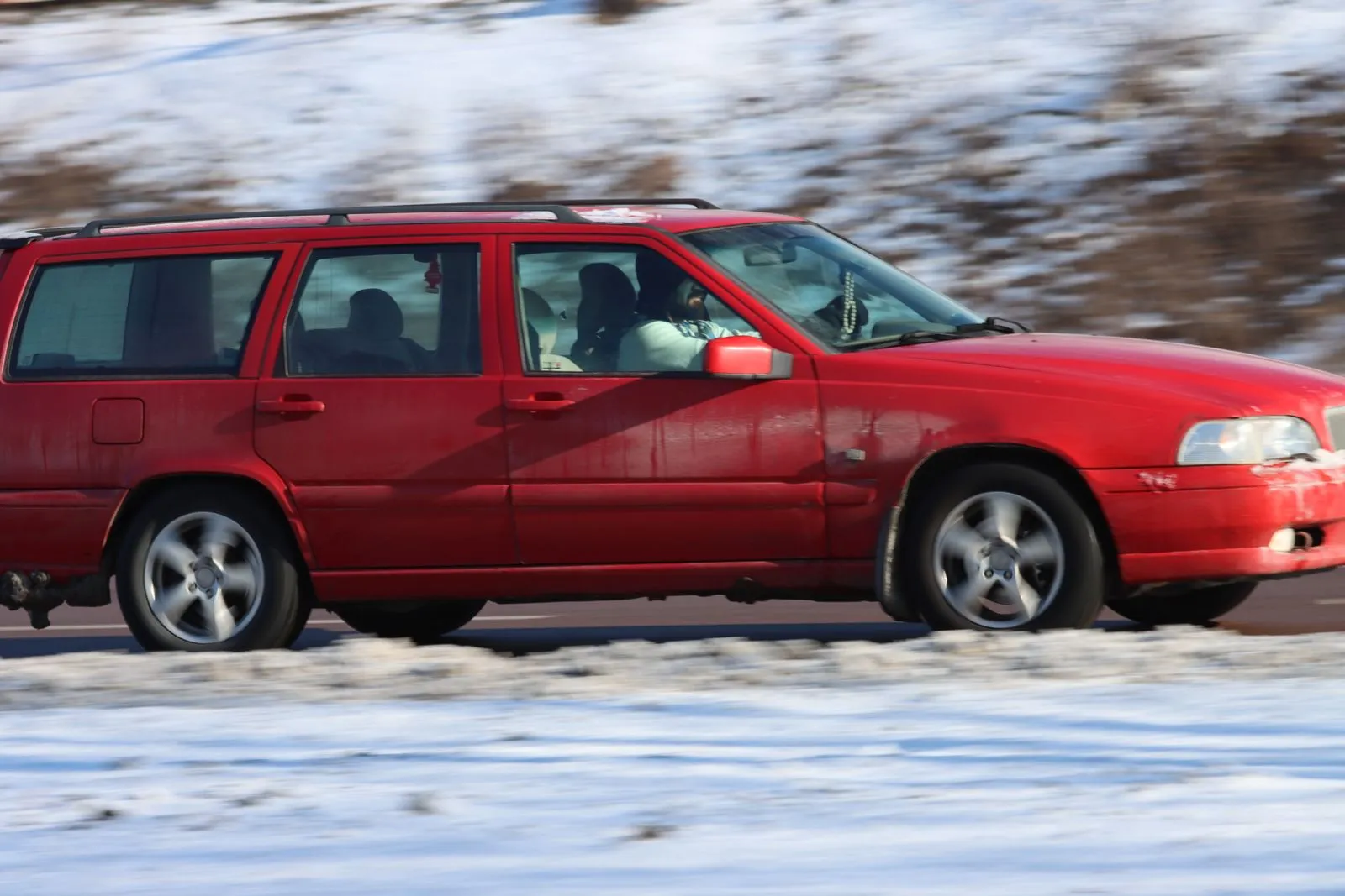 A red car in motion on a snowy road in Jönköping, Sweden, during winter.